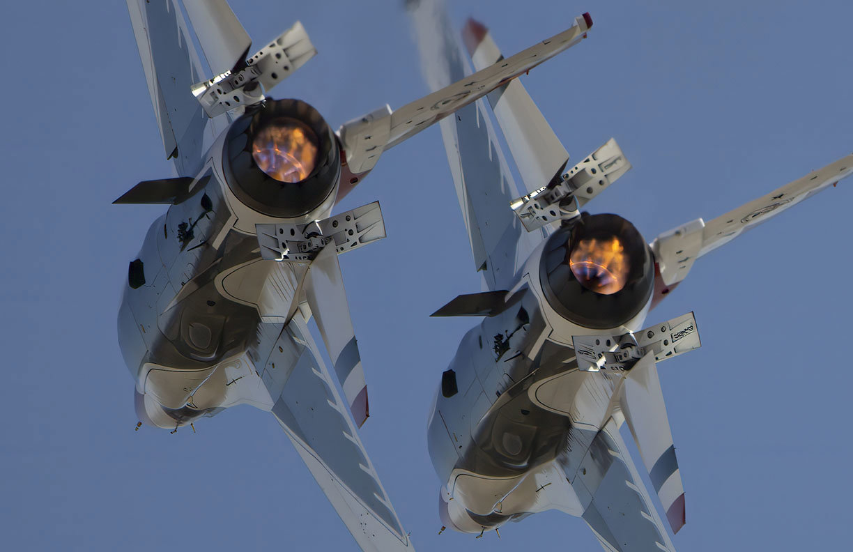 Two United States Air Force Thunderbirds F-16 fly in close formation from a dramatic underside perspective with brilliant afterburners lit and speed brakes deployed.