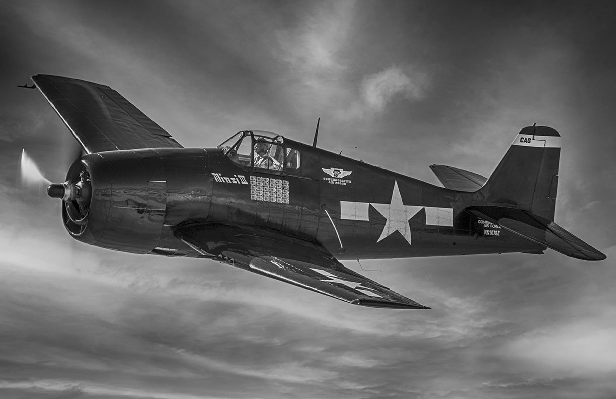 Commemorative Air Force F6F Hellcat warbird flying against a dramatic blue sky.